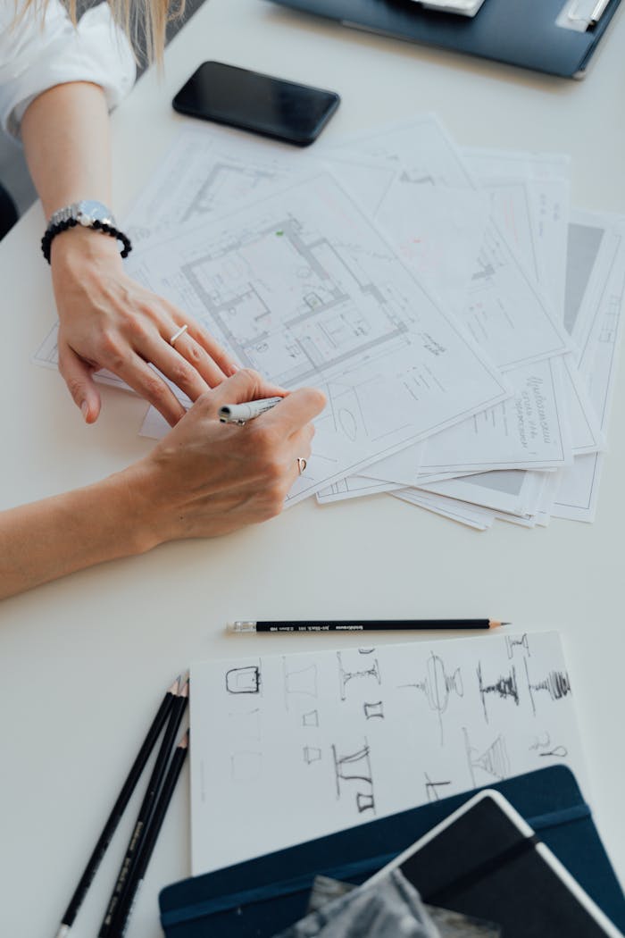 Hands of an architect drafting floor plans, surrounded by drawing tools and documents.